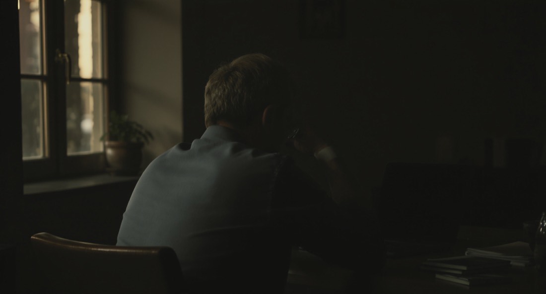 A man in his fifties at a desk turning his head and rolling one shoulder